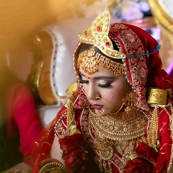 Traditional Indian bride in red and gold wedding attire with ornate jewelry and headpiece, captured in a close-up portrait by The Glorious Memories for bride photography in New Hyde Park, NY.