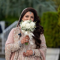 Bride in an embellished traditional outfit holding a white bouquet, photographed outdoors for The Glorious Memories bride photography in New Hyde Park, NY.